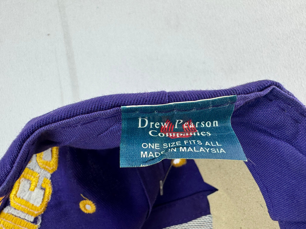 Close-up of a purple knit garment tag reading Drew Pearson Companies, with part of a gold-and-white embroidered letter visible on the fabric.