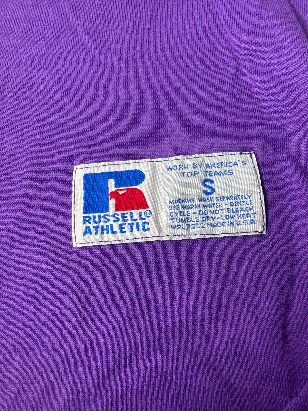 Close-up of a purple knit garment showing a sewn-on Russell Athletic brand label on the chest.