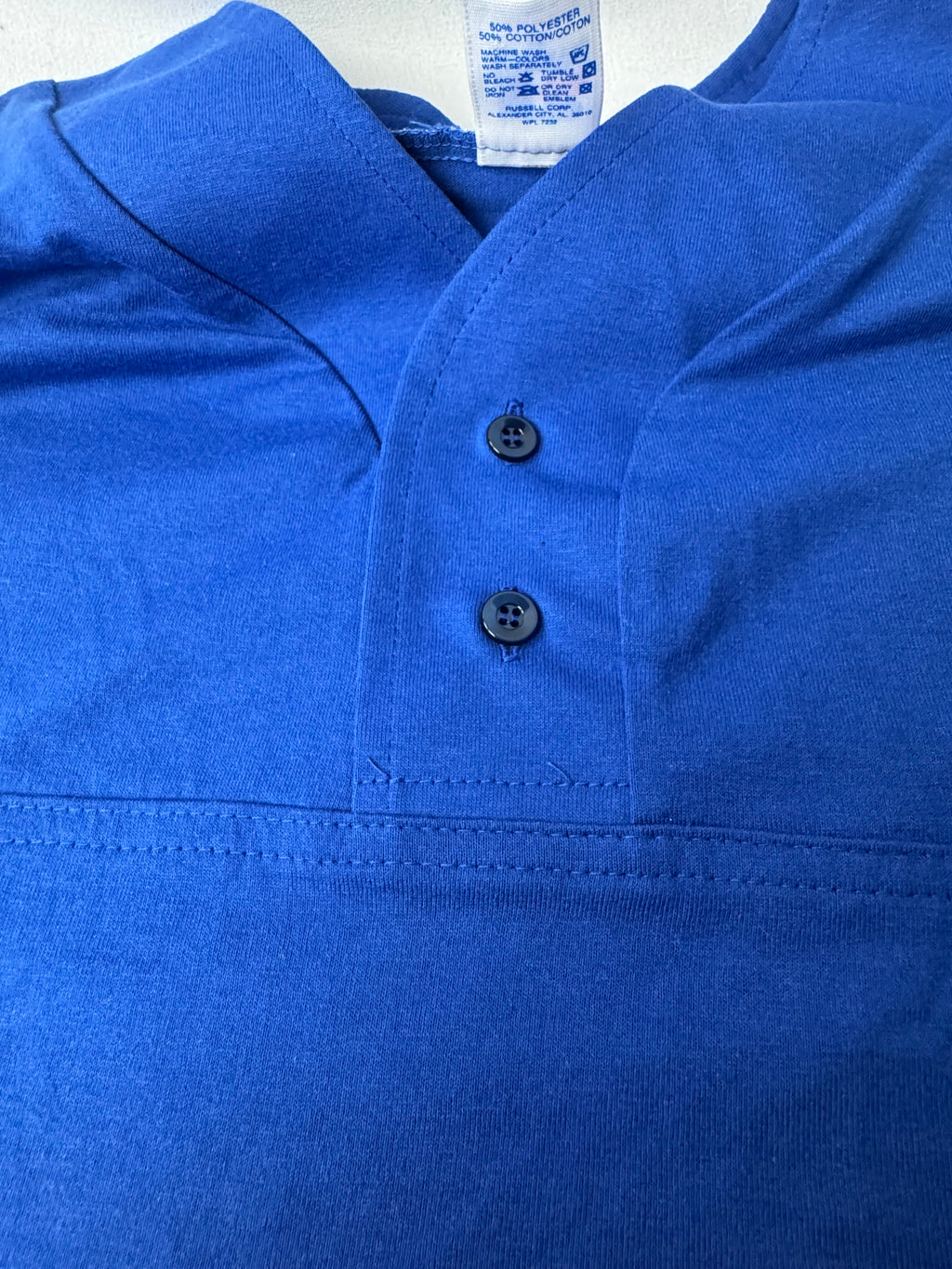 A close-up of a bright blue short-sleeve polo shirt with a two button placket and a visible Russell Athletic brand tag inside the collar.
