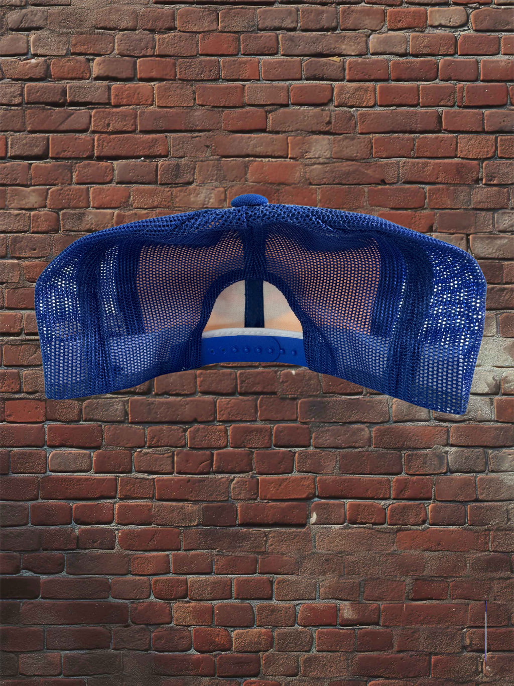 A blue mesh trucker-style baseball cap shown from the back, hanging against a red-brown brick wall.