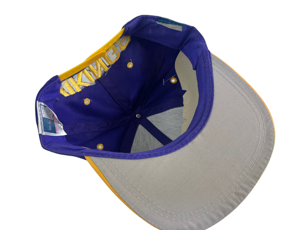 A vintage-style baseball cap shown from an angled top-down view, featuring a purple crown with gold embroidered lettering, a gray curved brim with a gold edge, and a gray mesh back.