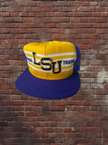 Vintage LSU Tigers AJD Superstripe hat with gold front, white stripes, and purple brim against a brick background