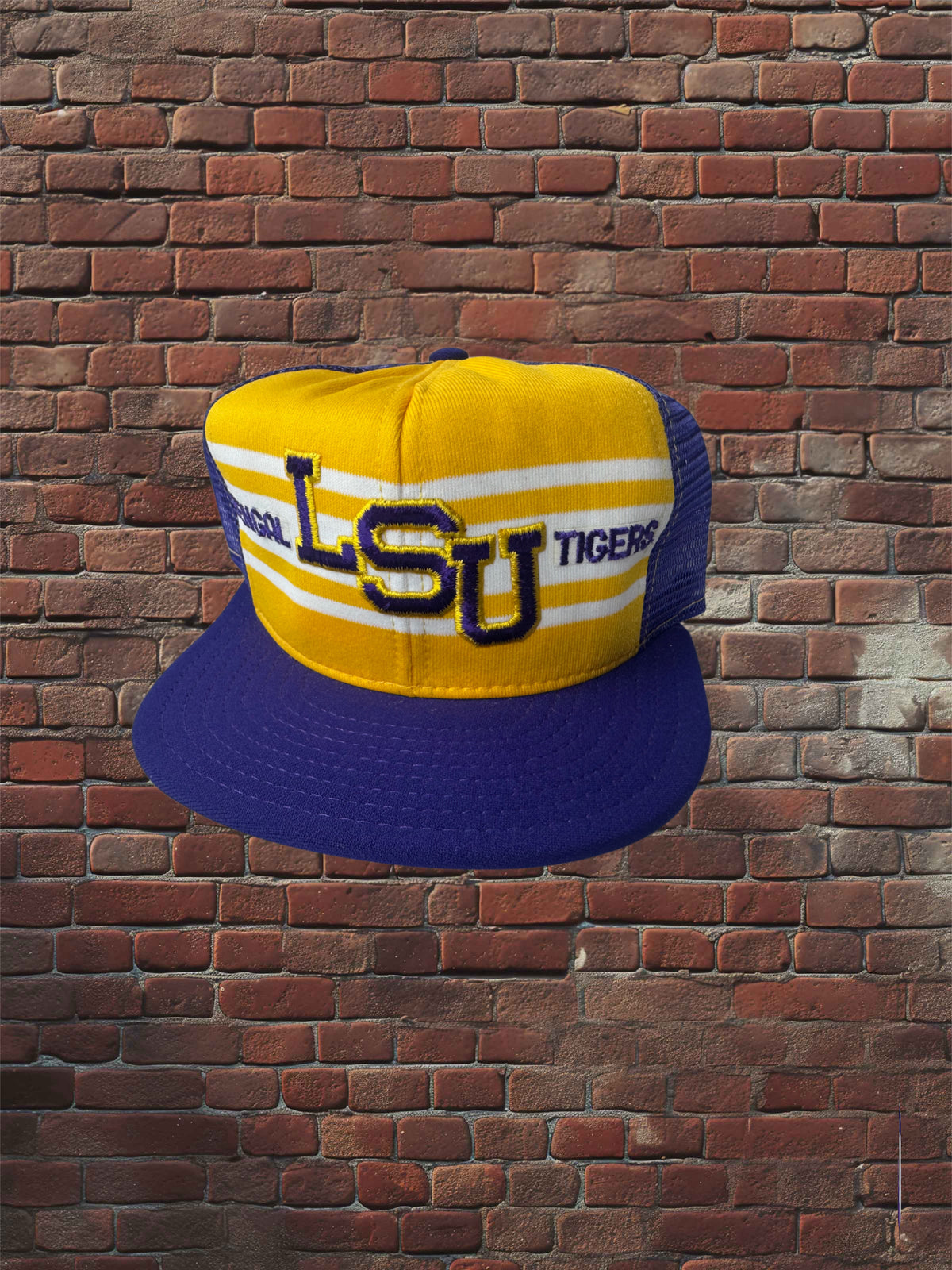 Vintage LSU Tigers AJD Superstripe hat with gold front, white stripes, and purple brim against a brick background