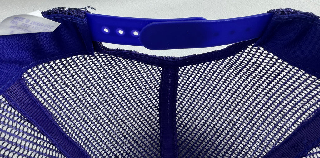 Close-up of the back of a purple trucker hat, showing the purple mesh back panels and adjustable plastic snapback closure.