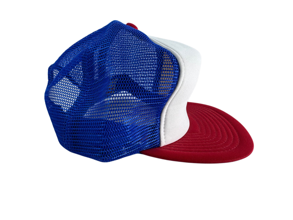 A three-color trucker cap with a royal blue mesh back, a white front panel, and a red flat brim, shown from a three-quarters angle on a white background.