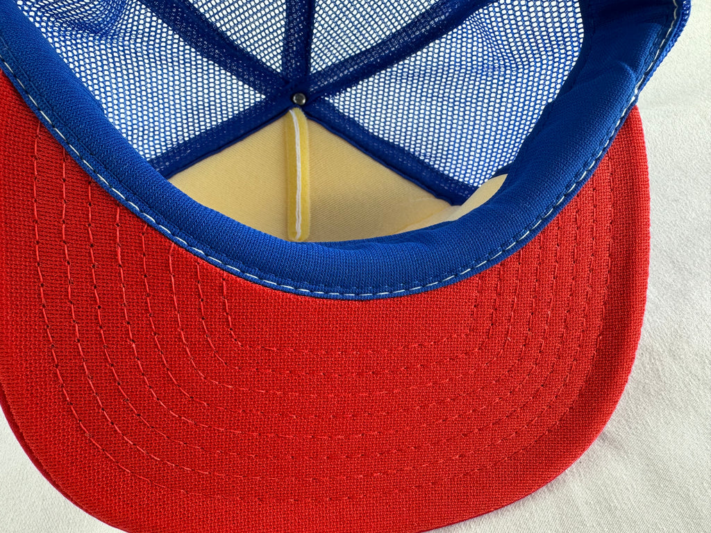Close-up of the back of a trucker-style cap showing a red fabric brim, blue mesh back panels, and blue stitched trim.