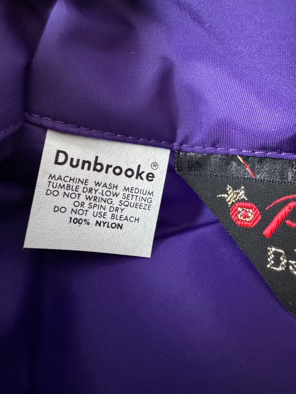 Close-up of a purple garment showing a white Dunbrooke care label and a black brand tag with red embroidery.
