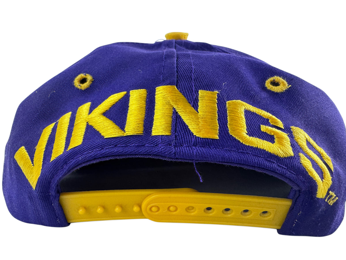 A purple and gold baseball cap featuring the word 'VIKINGS' embroidered in bold yellow letters across the front panels, with a gold snapback closure band visible at the back.