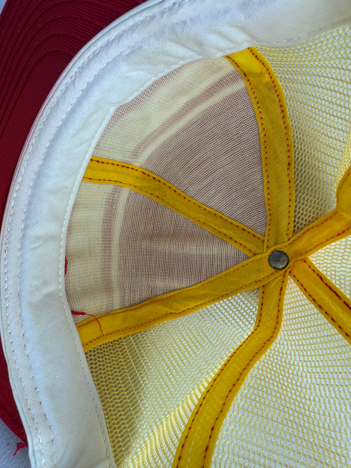 Close-up of the inside of a baseball cap showing a white fabric brim, white mesh crown panels, and yellow fabric panels radiating from a metal snap button.