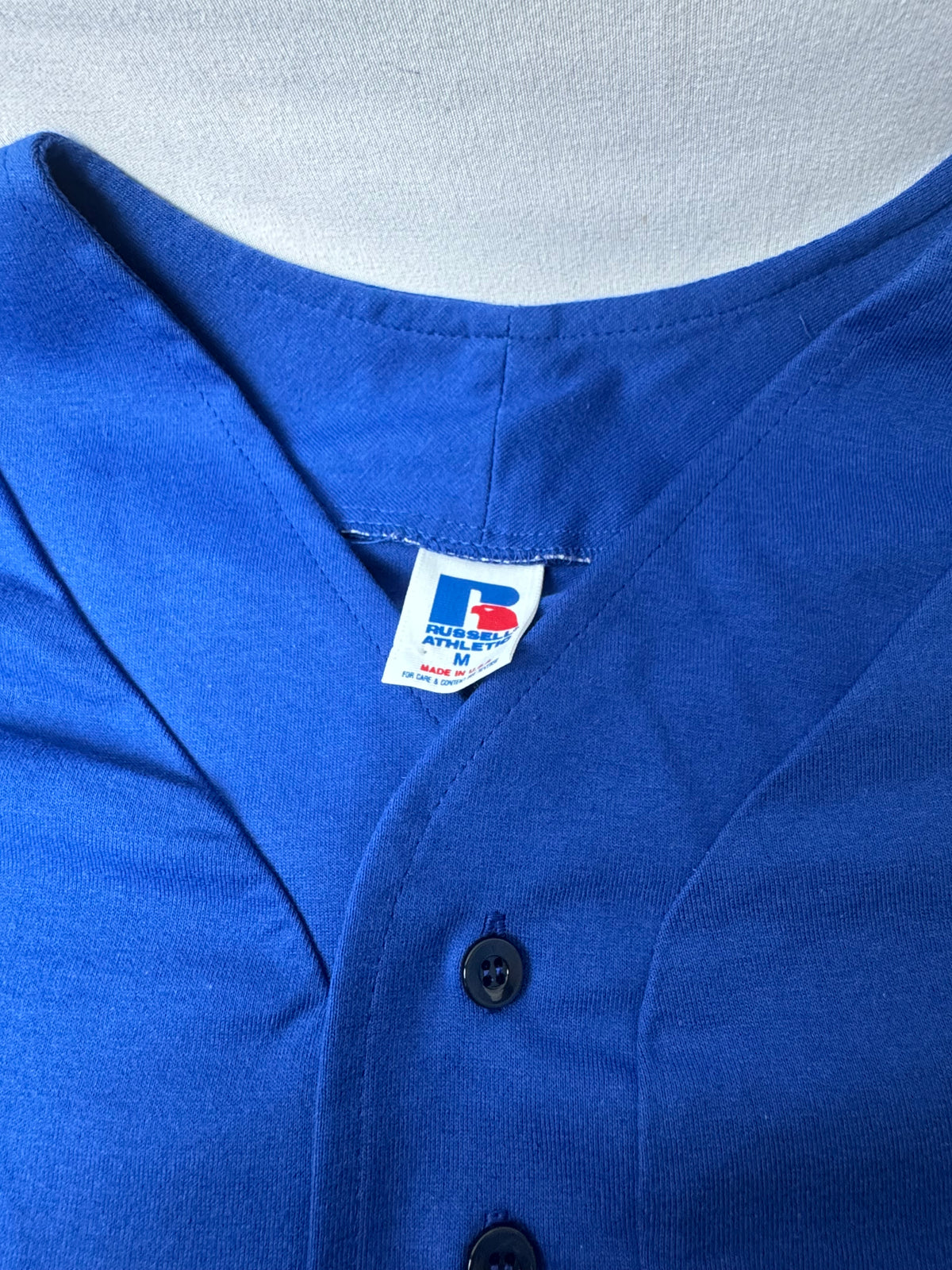 Close-up of a royal blue button-front shirt or top with a visible neck label reading Russell Athletic.