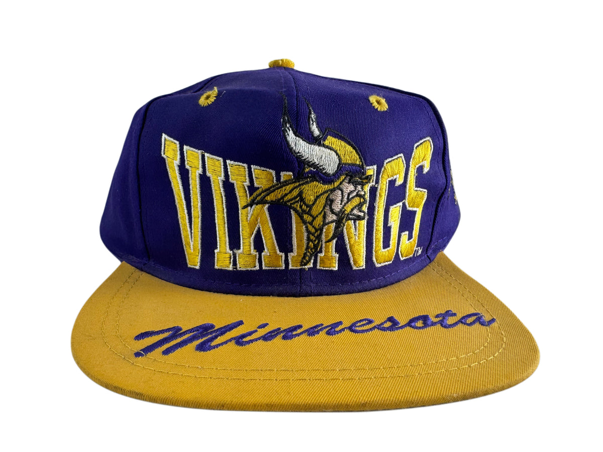A Minnesota Vikings snapback cap featuring a purple crown with yellow embroidered 'VIKINGS' text and the team logo, and a gold flat brim with 'Minnesota' written in purple script.