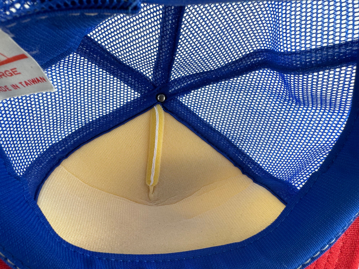 Close-up of the inside of a blue mesh trucker cap, showing the beige fabric sweatband, center seam, and a small portion of the red and white size label.