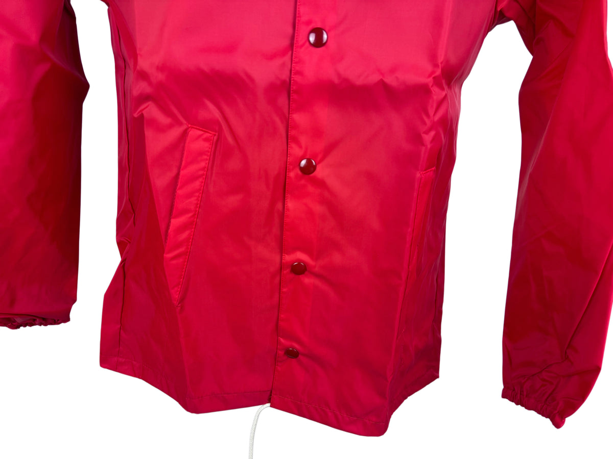 A close-up of a bright red jacket or windbreaker, showing the front button closure, side pocket, and elasticized cuffs against a plain white background.