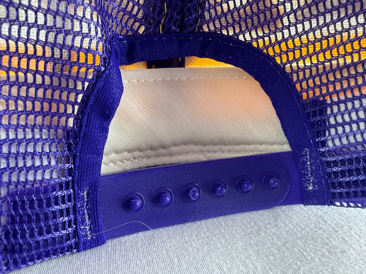 Close-up of the back of a purple mesh trucker hat, showing the adjustable snap closure and fabric panels.