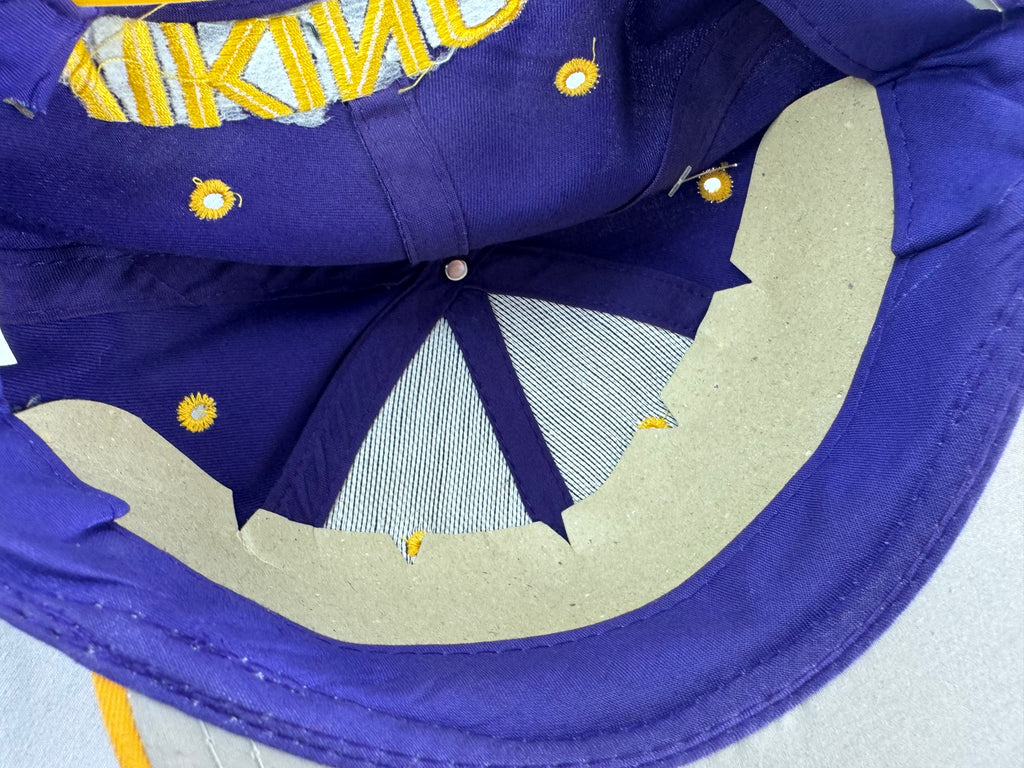 Close-up of the inside of a purple baseball cap with yellow embroidered lettering and small yellow sun motifs, showing the mesh back panel and construction details.
