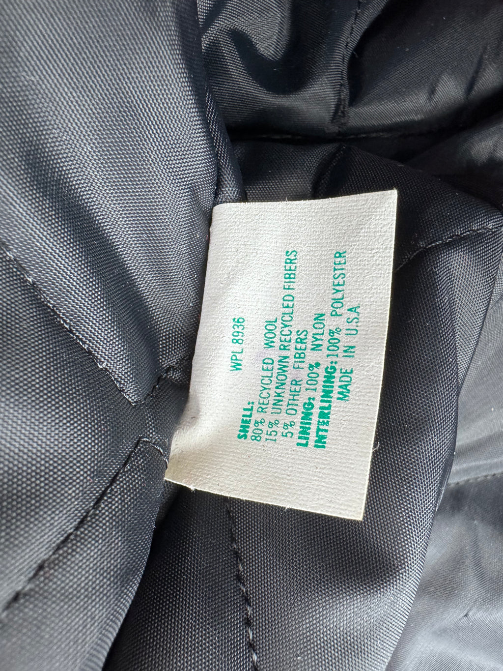 Close-up of a sewn-in fabric care label on a black quilted puffer jacket, showing material composition and 'MADE IN U.S.A.'