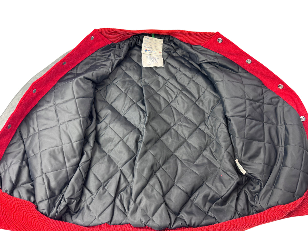 The interior of a red lettermen's jacket, showing the padded black lining, snap-button edge, and a small interior tag.