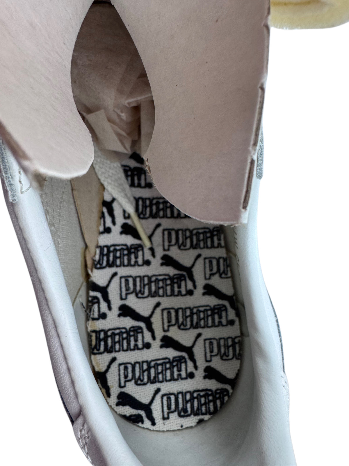 Close-up of the interior of a white Puma sneaker, showing the black and white Puma cat logo patterned insole and white laces.