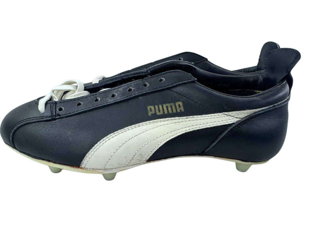 A single Puma leather soccer cleat in black and white, featuring the classic formstrip and gold Puma logo, shown from a side profile view on a white background.