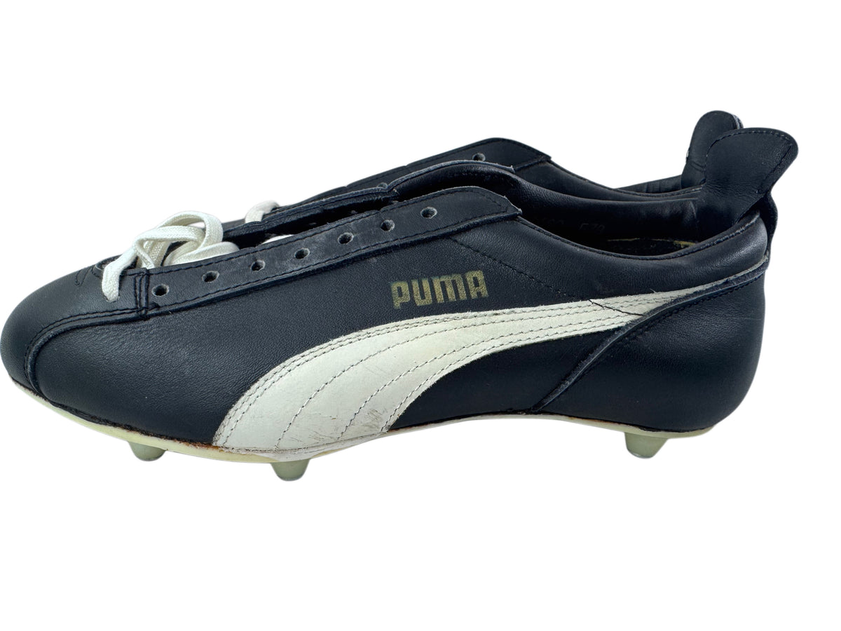 A single Puma leather soccer cleat in black and white, featuring the classic formstrip and gold Puma logo, shown from a side profile view on a white background.