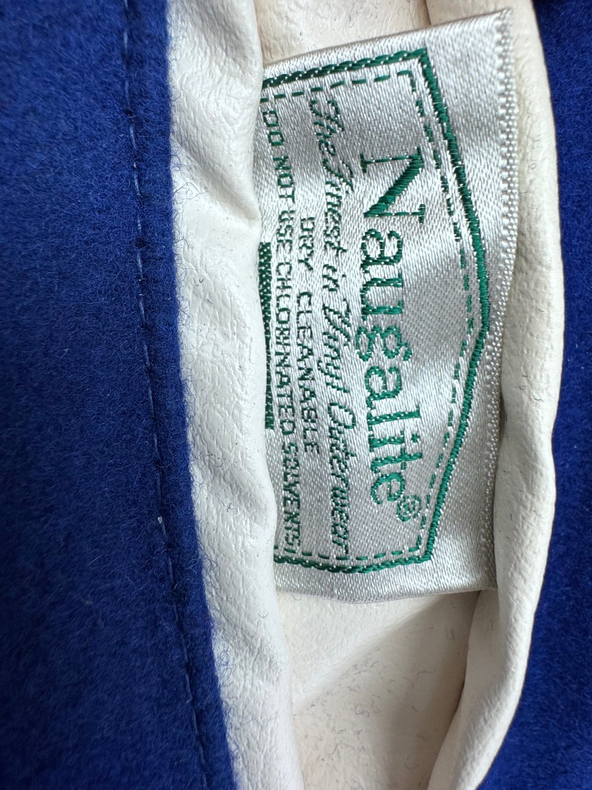 Close-up of a garment's inner label reading 'Naugaalite' with care instructions, shown against a blue and white fabric background.