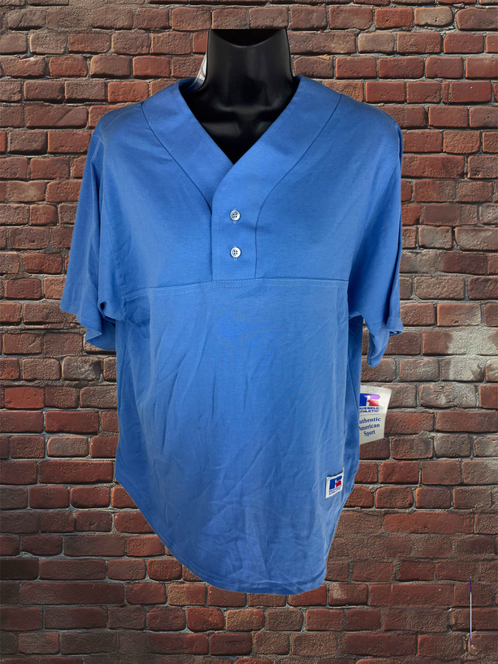 A blue short-sleeve V-neck athletic shirt displayed on a black mannequin torso against a red-brown brick wall background.