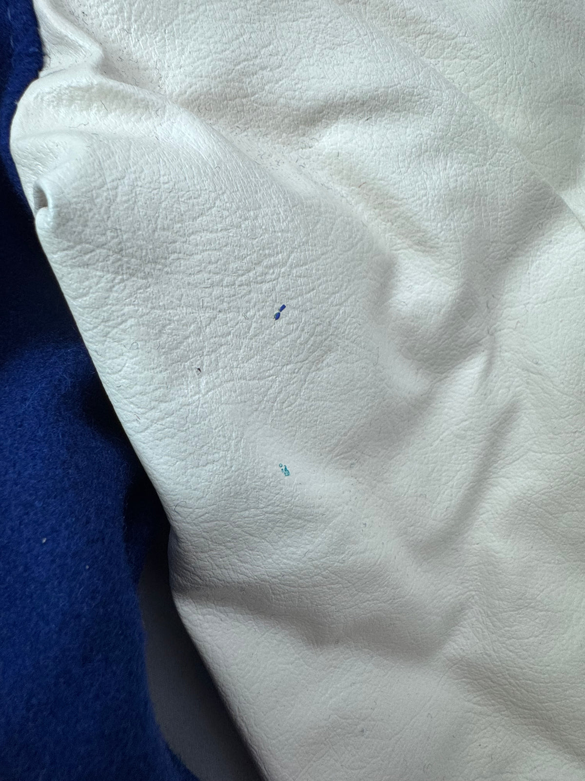 A close-up of a naugalite sleeve with a textured grain, showing small blue specks on the surface, with a dark blue fabric visible on the left edge.