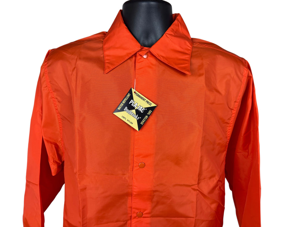 Bright orange long-sleeve snap-front closurenylon jacket with a pointed collar, displayed on a black mannequin torso against a white background. A black and gold 'Pla-Jac Dunbrooke' brand tag is attached to the chest.