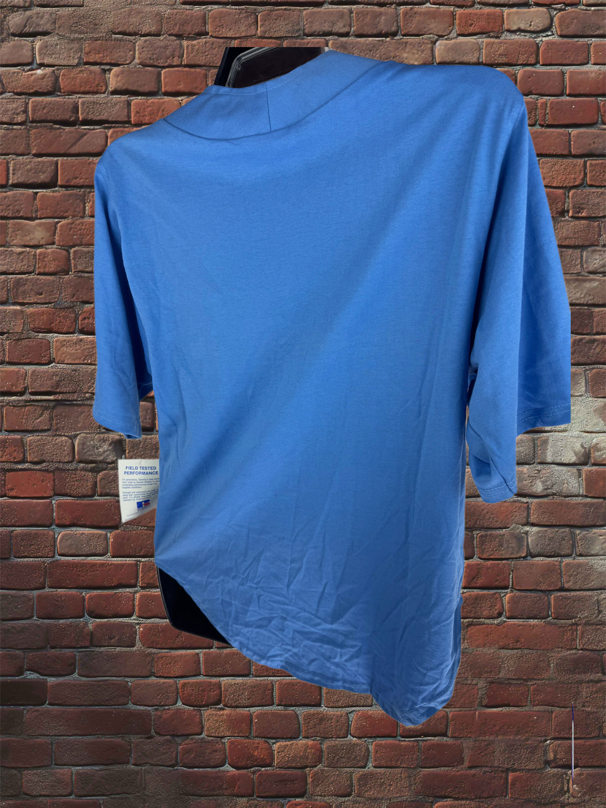 A bright blue short-sleeve t-shirt displayed on a black hanger against a red-brown brick wall background.