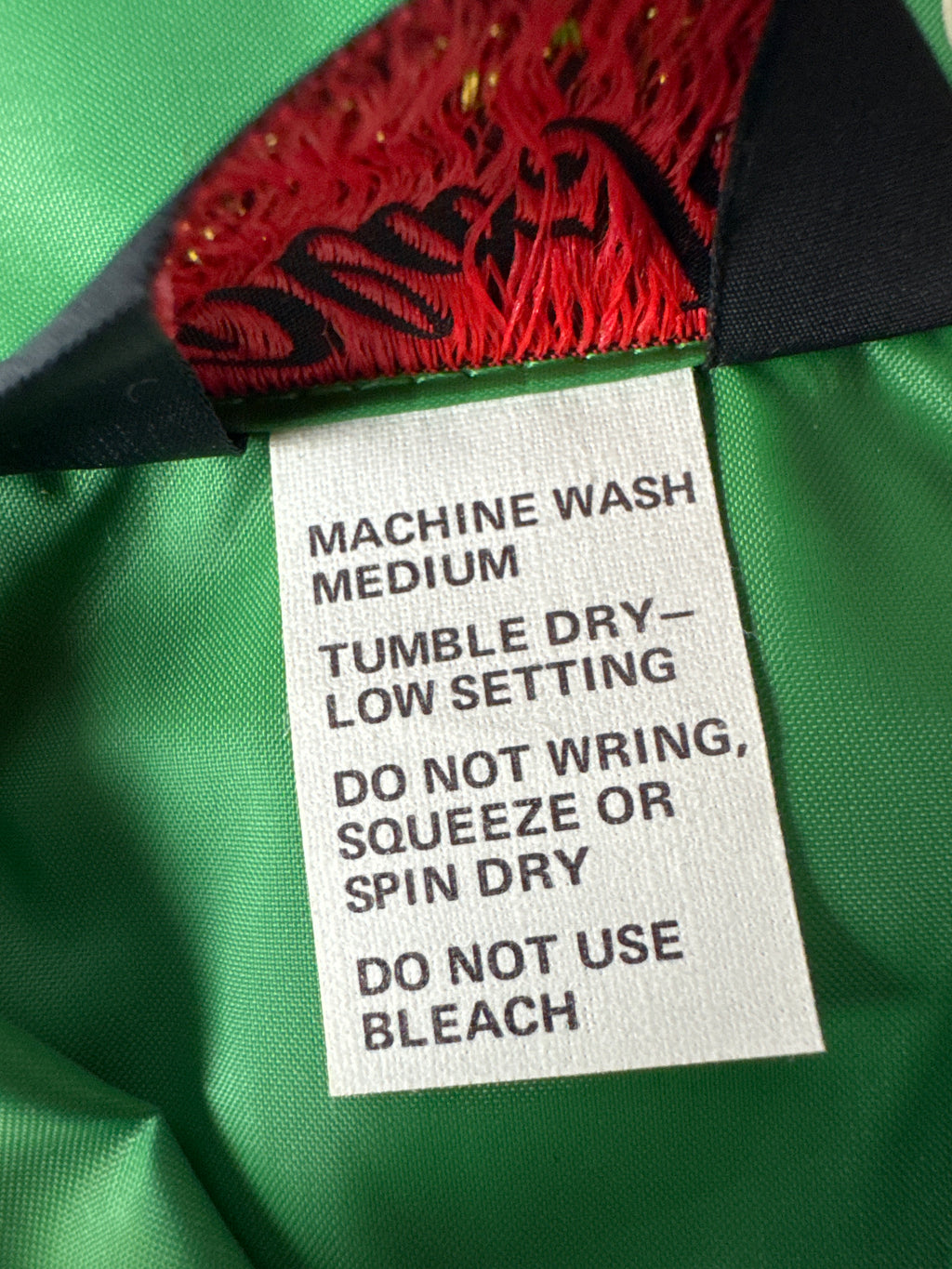 Close-up of a garment's interior label reading 'MACHINE WASH MEDIUM TUMBLE DRY - LOW SETTING DO NOT WRING, SQUEEZE OR SPIN DRY DO NOT USE BLEACH' on a green fabric background with red and black embroidery.