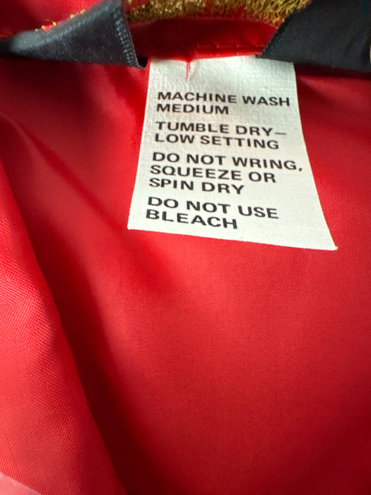 A close-up of a garment's inner neck label reading 'MACHINE WASH MEDIUM TUMBLE DRY - LOW SETTING DO NOT WRINK, SQUEEZE OR SPIN DRY DO NOT USE BLEACH' against a bright red fabric background.