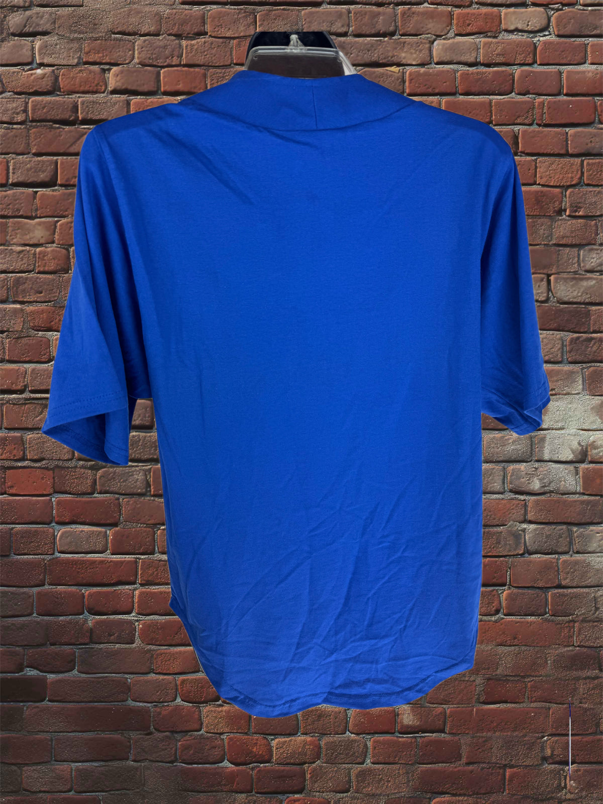 A royal blue short-sleeve t-shirt displayed on a hanger against a red-brown brick wall background.