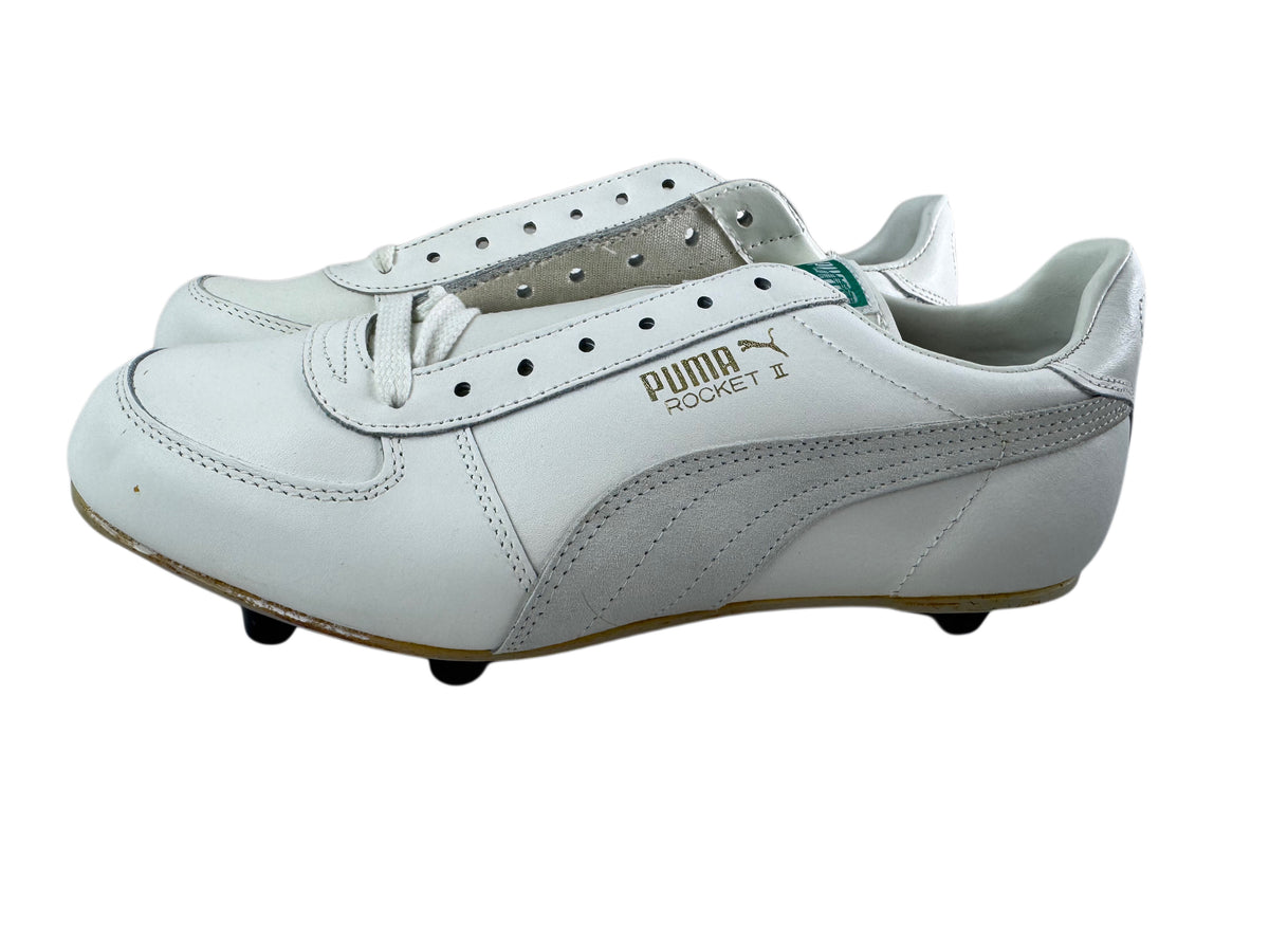 A pair of white Puma Rocket II cleats with silver side stripes and gold branding, shown from a side profile view on a white background.