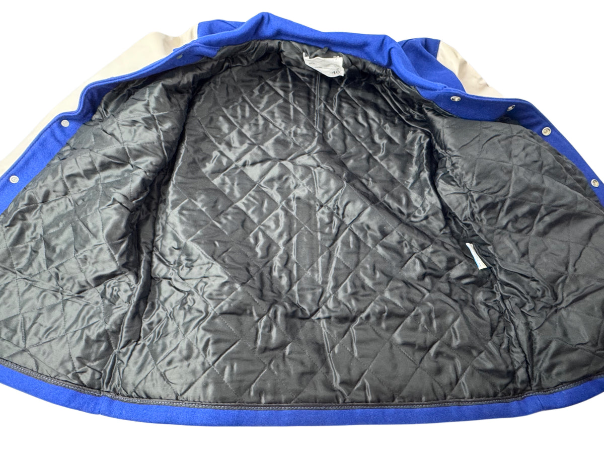 A vintage lettermen's jacket shown open, displaying a thick black diamond-quilted interior lining and blue trim with white sleeves.