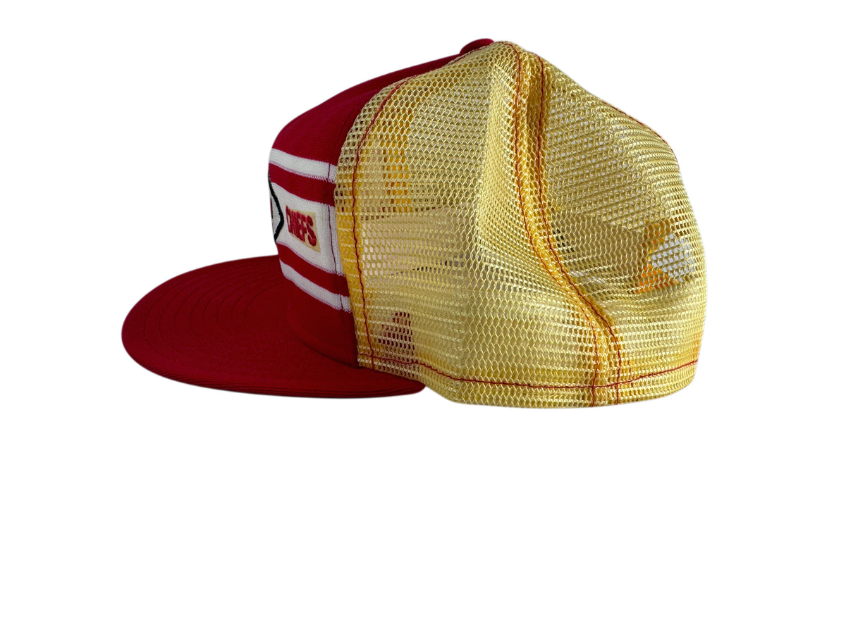 A red and gold trucker hat with a red flat brim, red front panel, white and red stripes, and a gold mesh back.