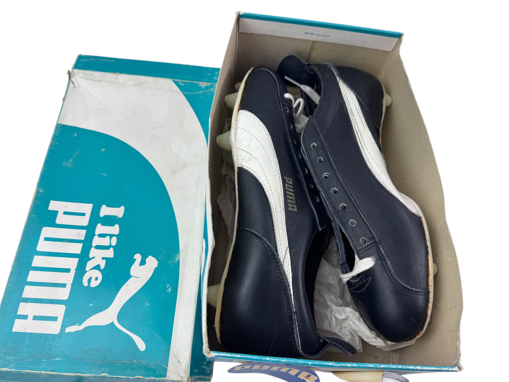A pair of Puma soccer cleats in black and white leather, shown inside their original teal and white Puma shoebox on a white background.