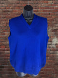 A bright royal blue ribbed knit sweater vest displayed on a black mannequin torso, set against a red-brown brick wall background.