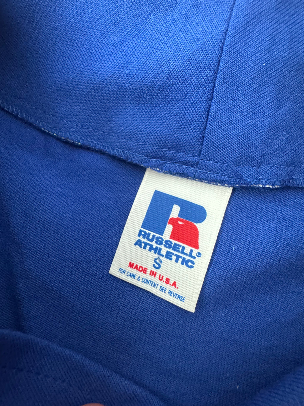 Close-up of a blue Russell Athletic garment showing the interior neck label with the brand logo and 'Made in U.S.A.' text.