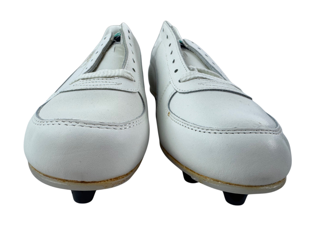 A pair of white leather soccer/football shoes with black plastic studs, shown from a front-facing perspective against a white background.