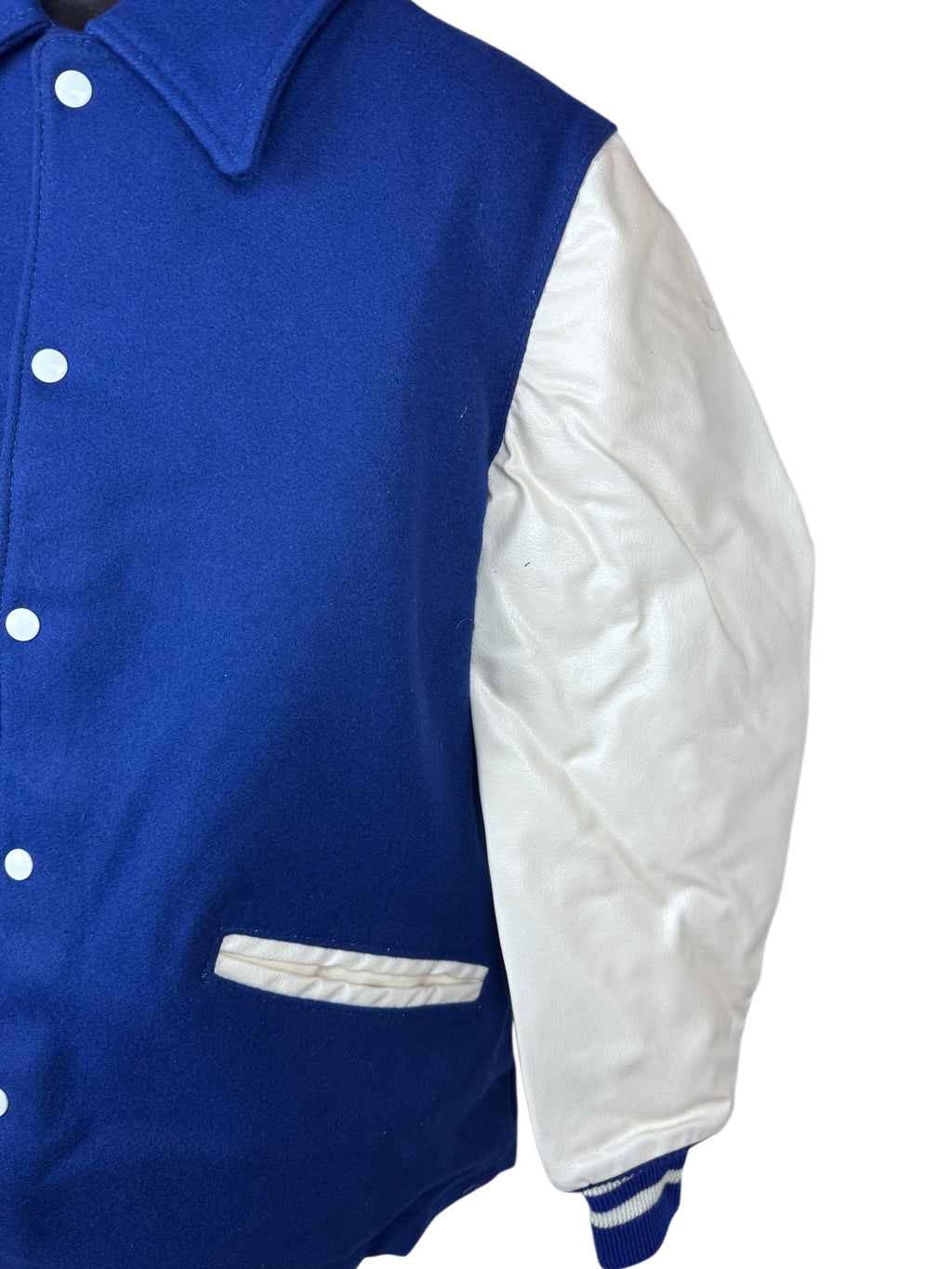A close-up of a varsity-style jacket with a royal blue body and white sleeves, showing the front buttons, collar, and a white pocket.