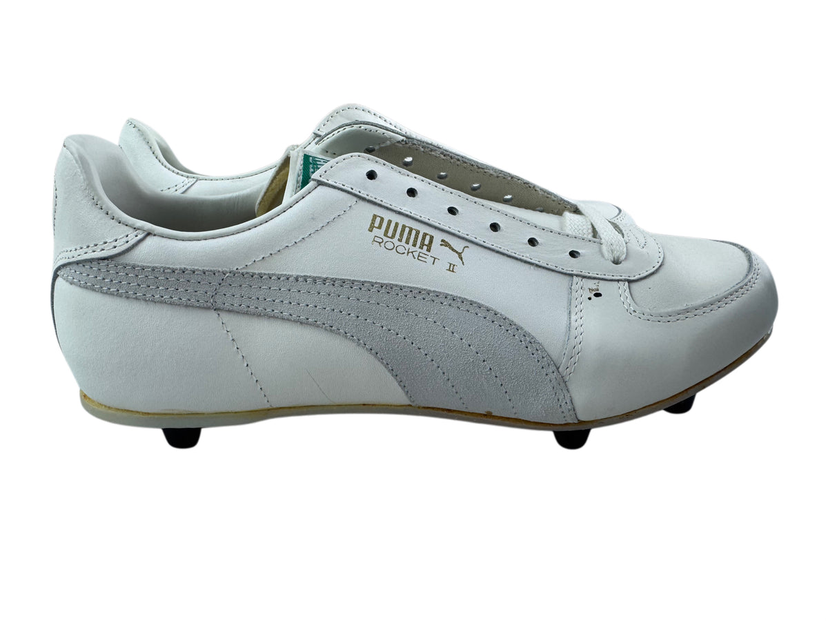 A white Puma Rocket 2 soccer shoe with light gray suede overlays and gold branding on the side, shown against a plain white background.