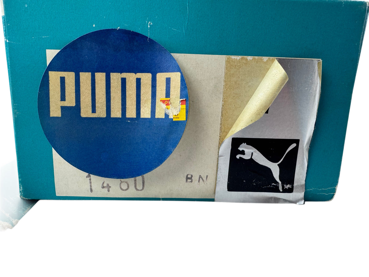 A vintage teal Puma shoebox with a large blue circular Puma logo sticker on the front, alongside a peeled-back silver protective film revealing a black Puma cat logo sticker underneath.