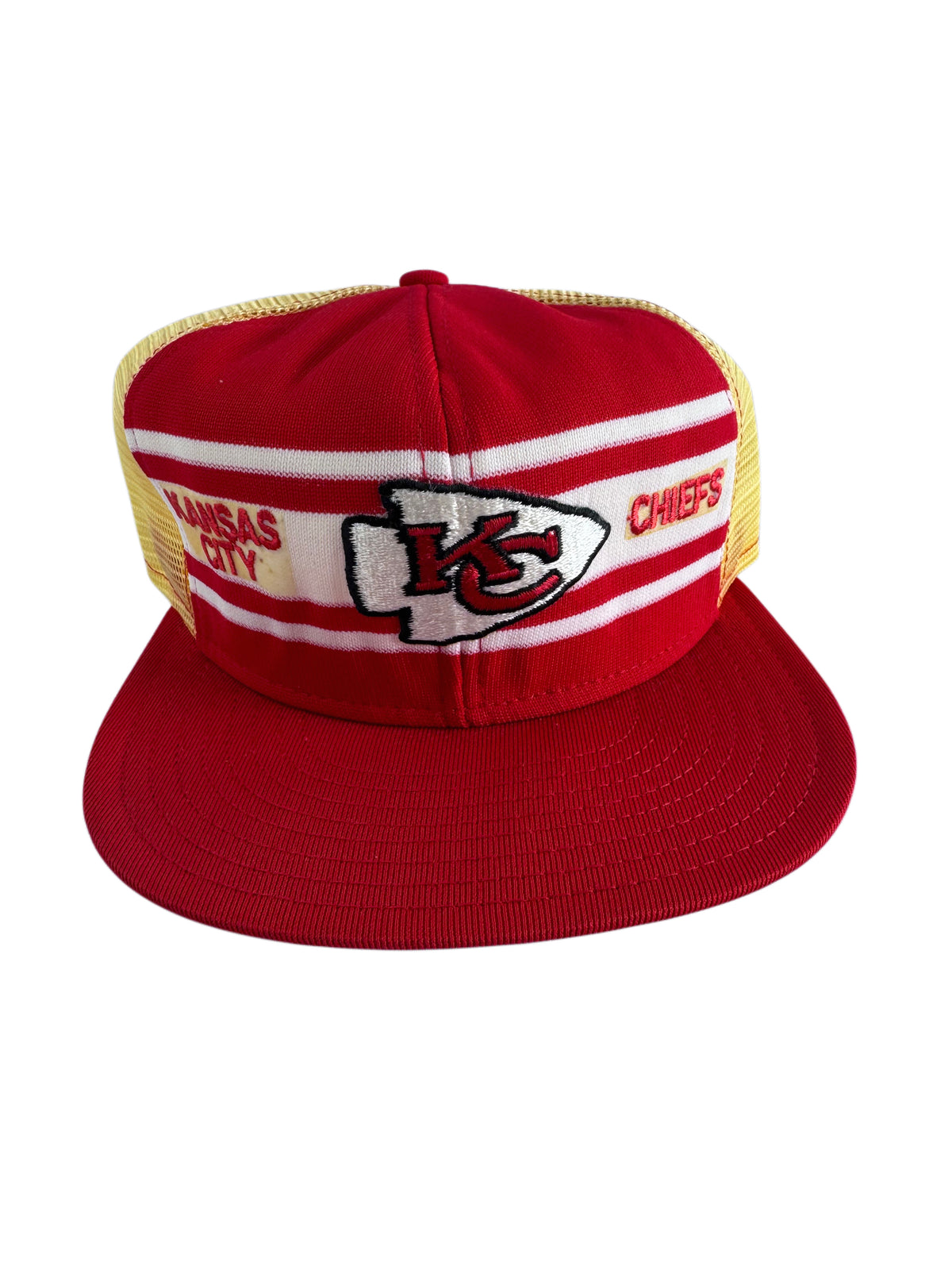 A red and white Kansas City Chiefs trucker hat with a red flat brim, red front panels, white stripes, and yellow mesh back panels. The front features the embroidered Kansas City Chiefs logo and text.