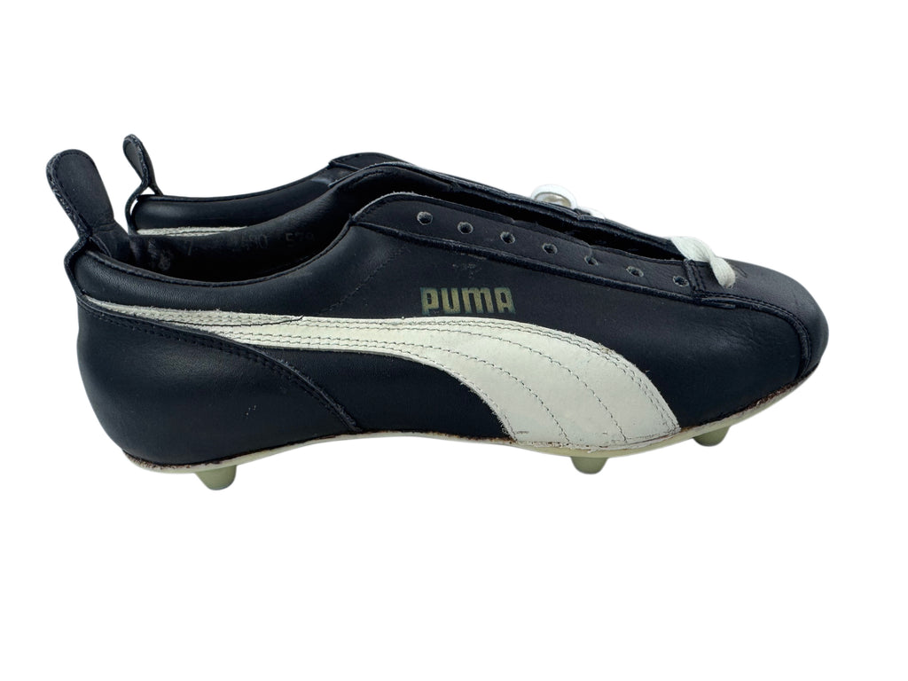 A single Puma leather soccer cleat in black and white, featuring a black upper, a white side stripe, and a white Puma logo printed on the side. The shoe has a pull tab at the heel and small plastic studs on the sole, shown against a plain white background.