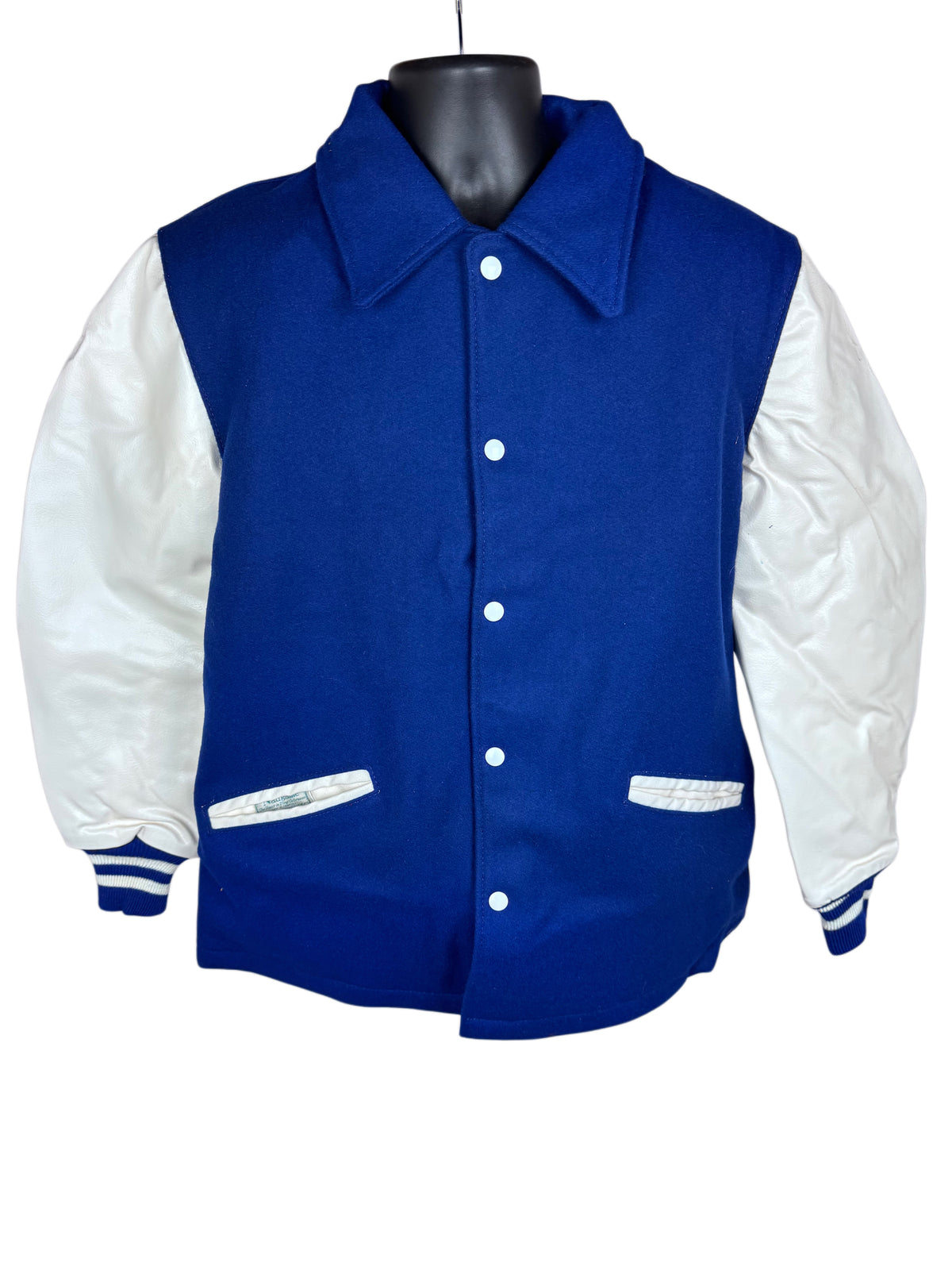 A classic varsity jacket with a royal blue wool body and white leather sleeves, displayed on a black mannequin torso against a white background.
