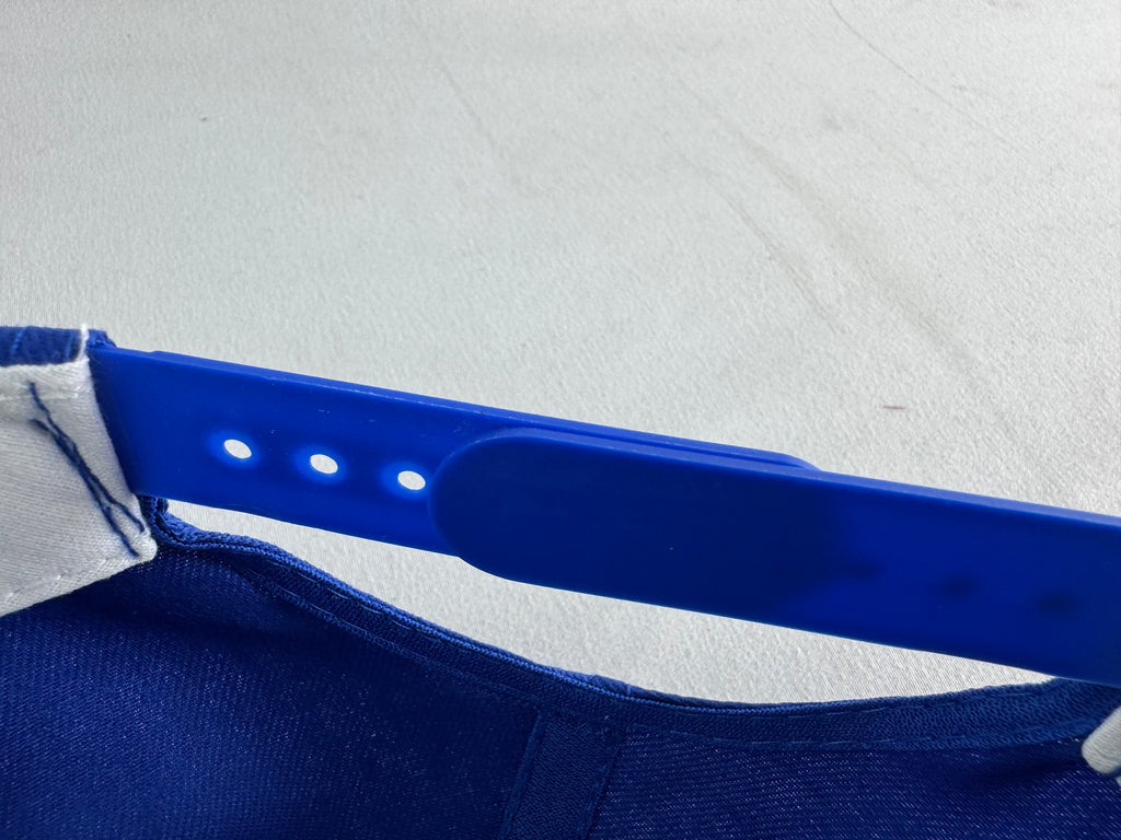 A close-up of a blue adjustable strap, likely a neck strap or band shown attached to a dark blue garment against a light gray background.