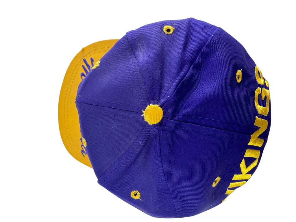 A purple and yellow baseball cap shown from a side angle, featuring yellow embroidered lettering on the side and yellow eyelets, with a yellow brim visible in the background.