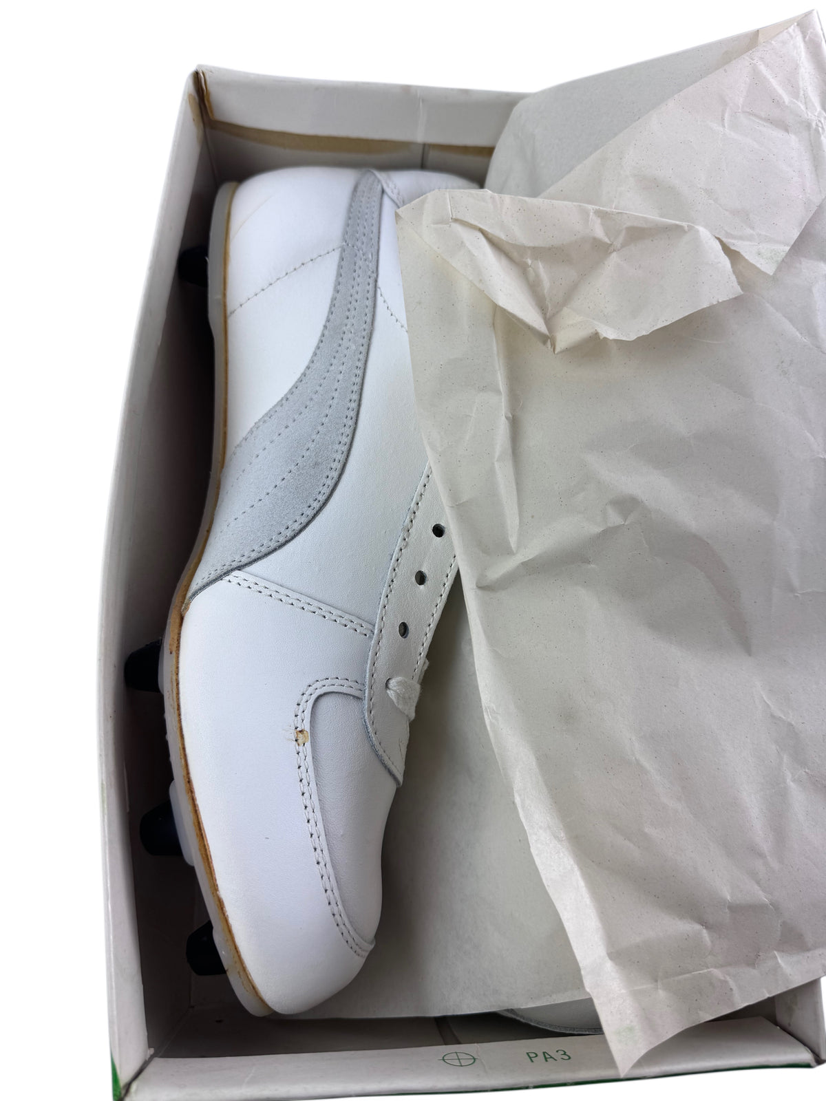 A white leather soccer/football shoe partially tucked inside an open shoebox with tissue paper visible, photographed on a white background