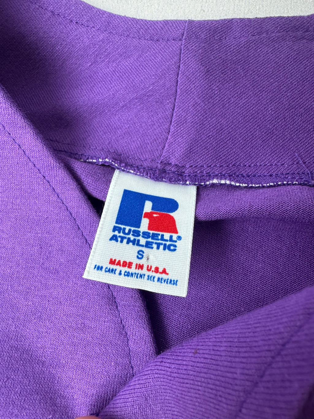 Close-up of a purple athletic garment showing a Russell Athletic size S neck label.