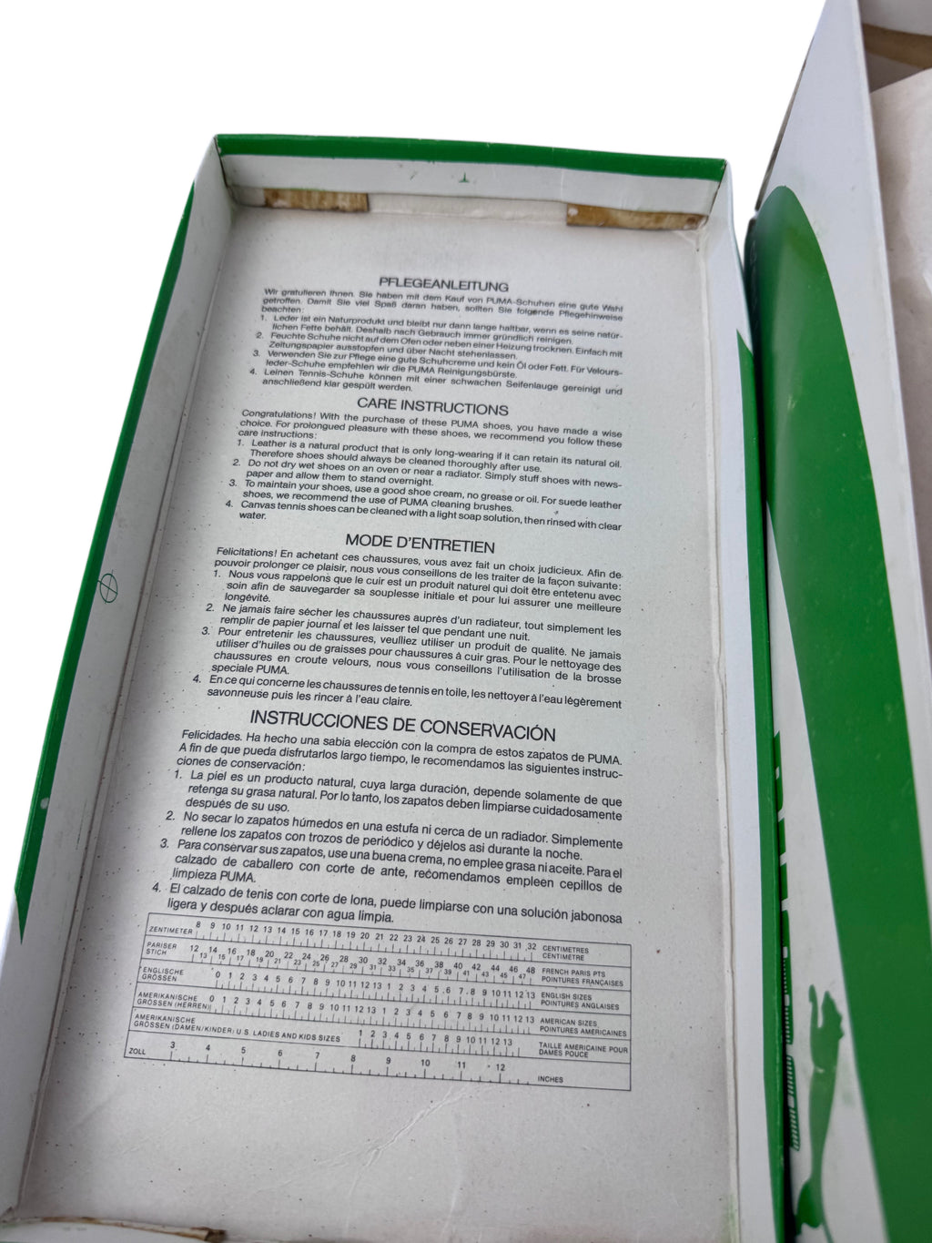The inside of a green and white box showing printed care and conservation instructions in multiple languages on a white insert, with a green patterned sheet partially visible on the right.